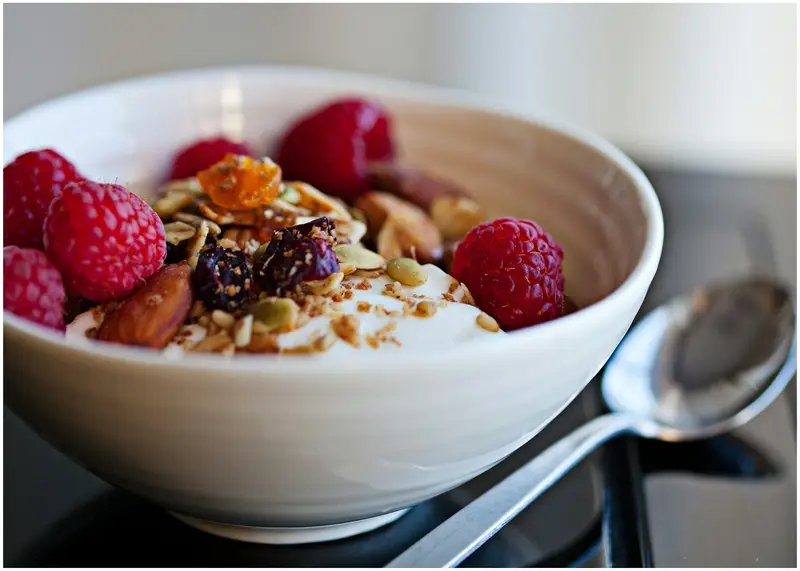 A bowl of granola topped with raspberries and nuts