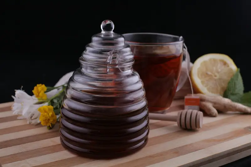 A jar of honey next to a cup of tea on a cutting board