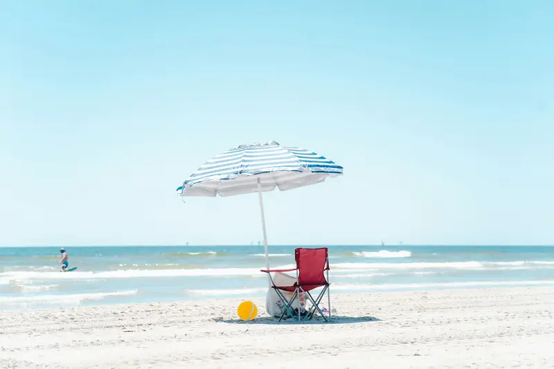 A beach umbrella shading a chair on a bright, sunny beach