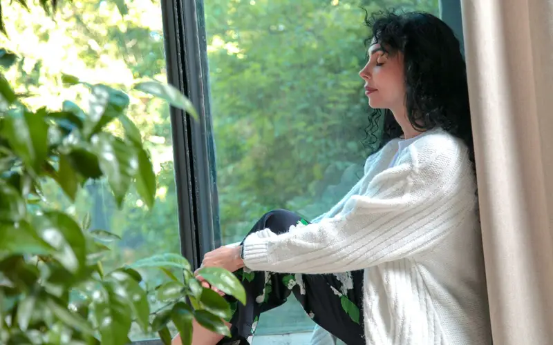 A woman sitting on a window sill, looking out calmly
